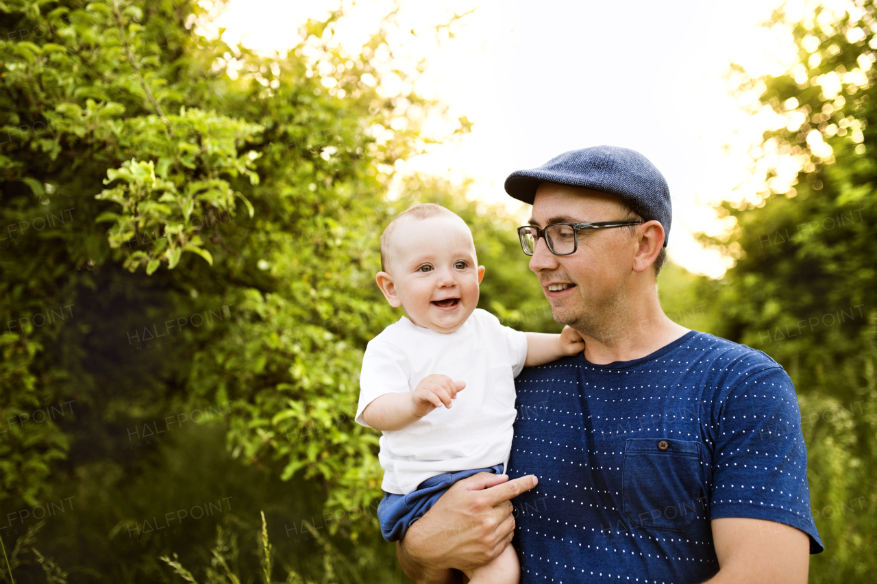 Young father in green summer nature holding his cute baby son in the arms.