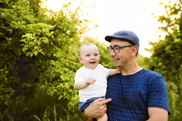 Young father in green summer nature holding his cute baby son in the arms.