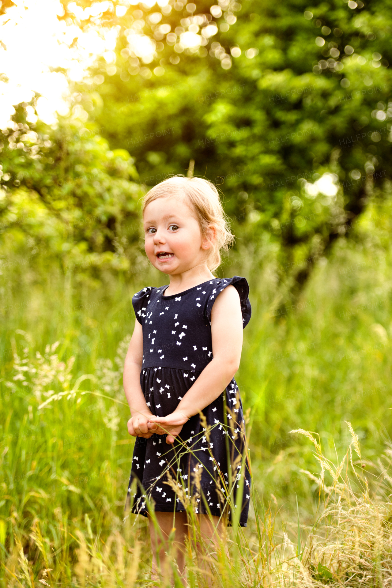 Cute little blonde girl in blue dress outside in in green sunny summer nature