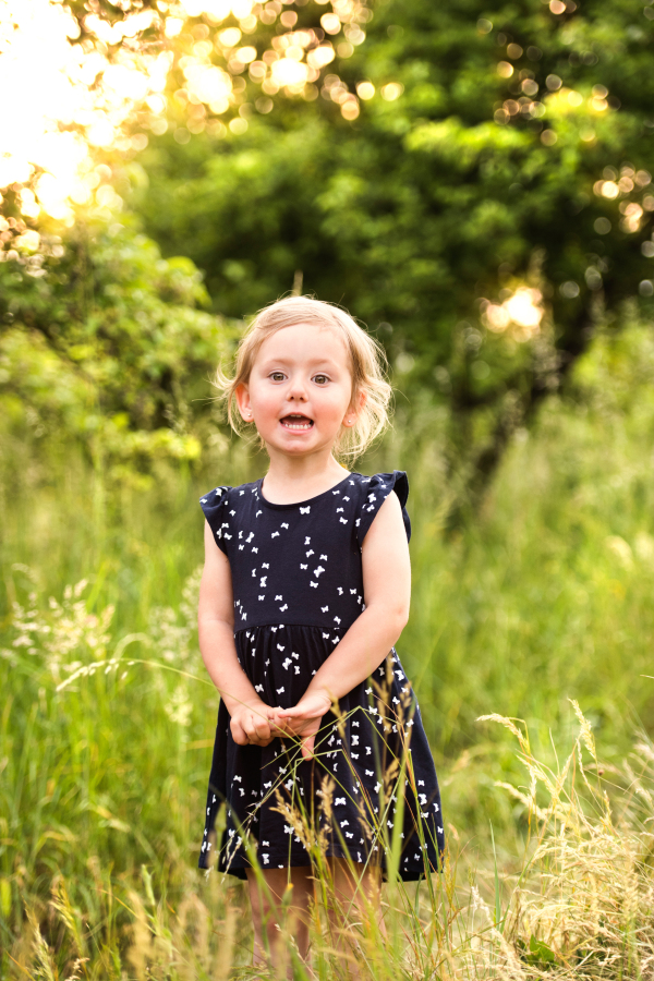 Cute little blonde girl in blue dress outside in in green sunny summer nature