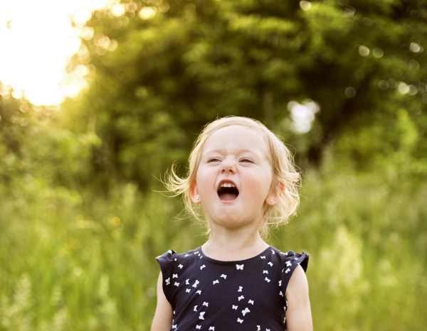 Cute little blonde girl in blue dress outside in in green sunny summer nature