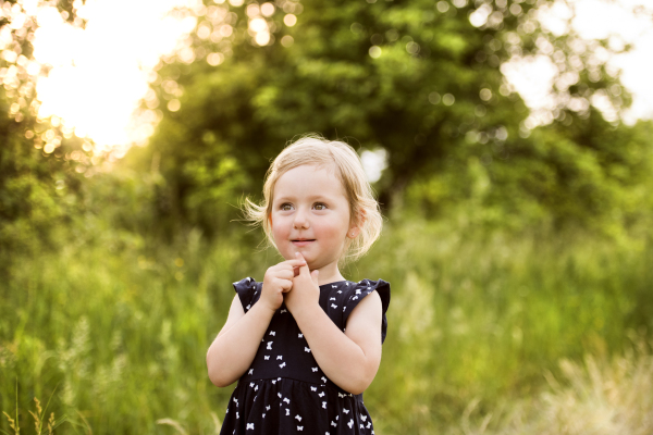 Cute little blonde girl in blue dress outside in in green sunny summer nature