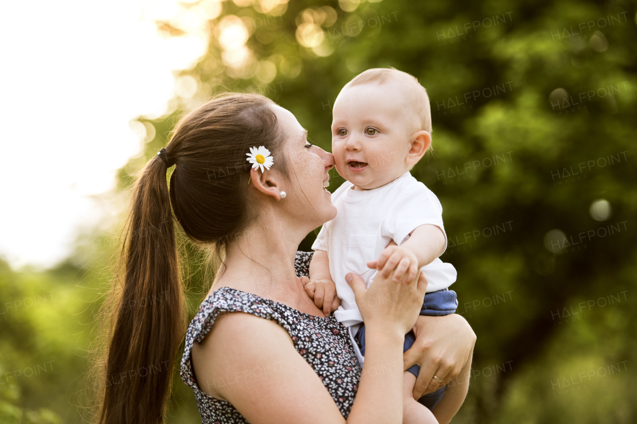 Beautiful young mother in green sunny summer nature holding baby son in the arms.