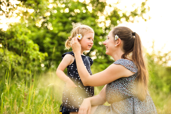 Beautiful young mother in green sunny summer nature holding her cute little daughter in the arms.