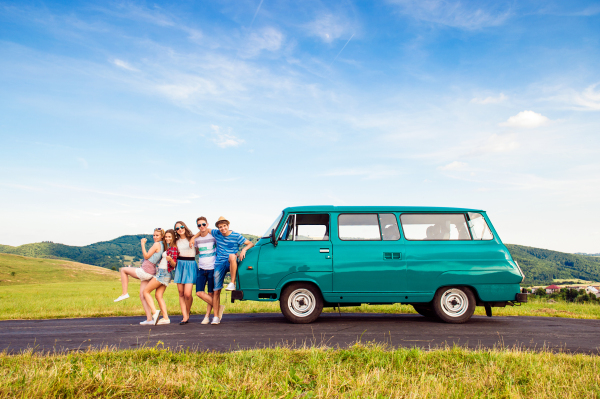 Young teenage hipster frieds with campervan against green nature and blue sky