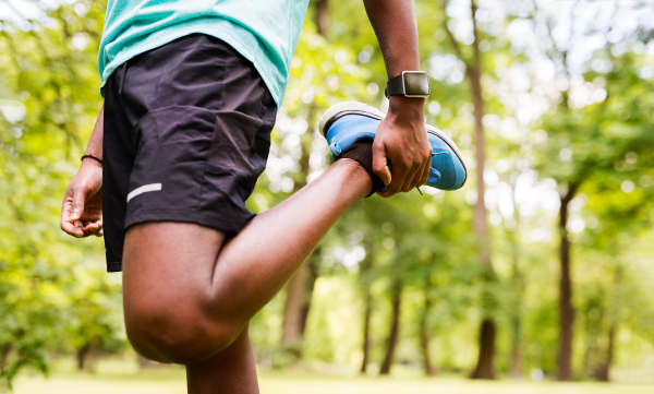 Unrecognizable afro-american man in park warming up and stretching arms and legs before training.