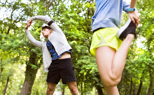 Running couple in park warming up and stretching arms and legs before training.