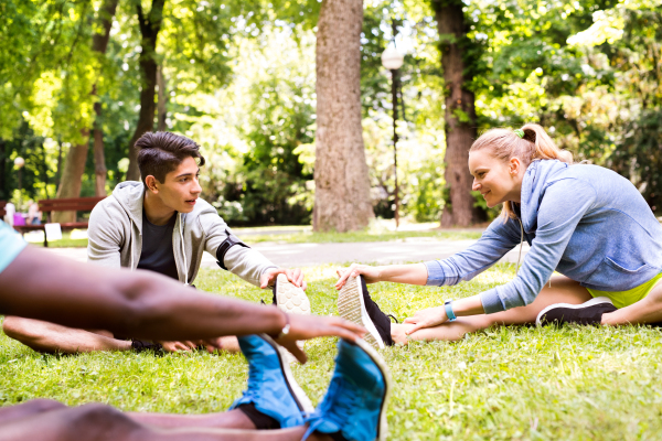 Group of young runners in nature, sitting on grass, warming up and stretching legs