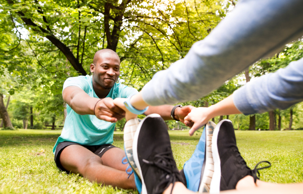 Running couple in park sitting on the grass, warming up and stretching arms and legs before training.