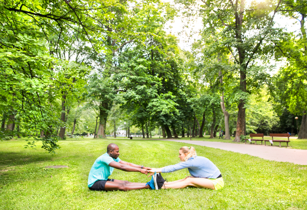 Running couple in park sitting on the grass, warming up and stretching arms and legs before training.