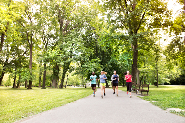 Group of young athletes running in green sunny summer park.