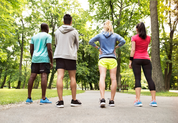 Group of young athletes prepared for run in green sunny summer park, rear view.