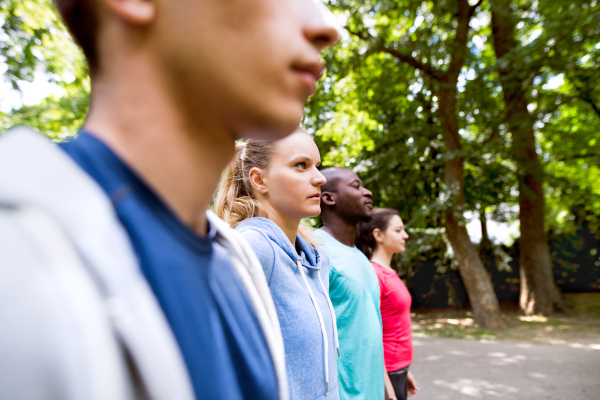 Group of young athletes prepared for run in green sunny summer park.