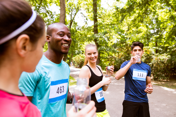 Group of young athletes prepared for run in green sunny summer park, holding bottles, drinking water.