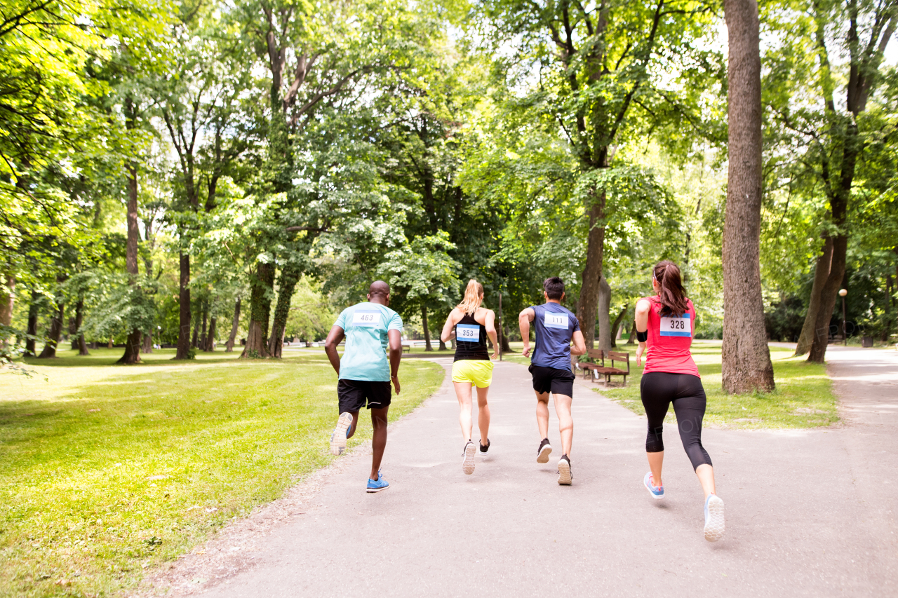 Group of young athletes running in green sunny summer park.