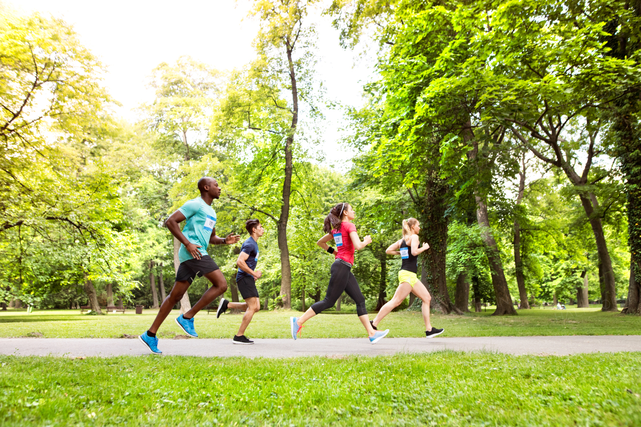 Group of young athletes running in green sunny summer park.