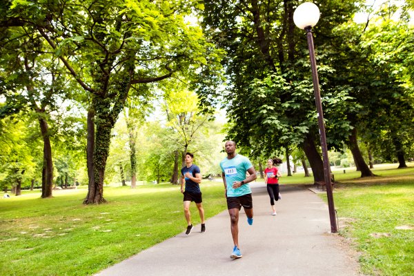 Group of young athletes running in green sunny summer park.