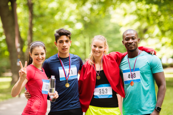 Group of young fit friends at the finish line happy after completing race. Green sunny park.