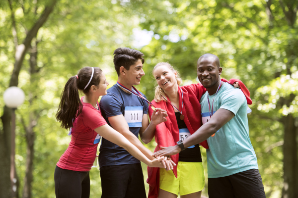 Group of young fit friends at the finish line happy after completing race. Green sunny park.