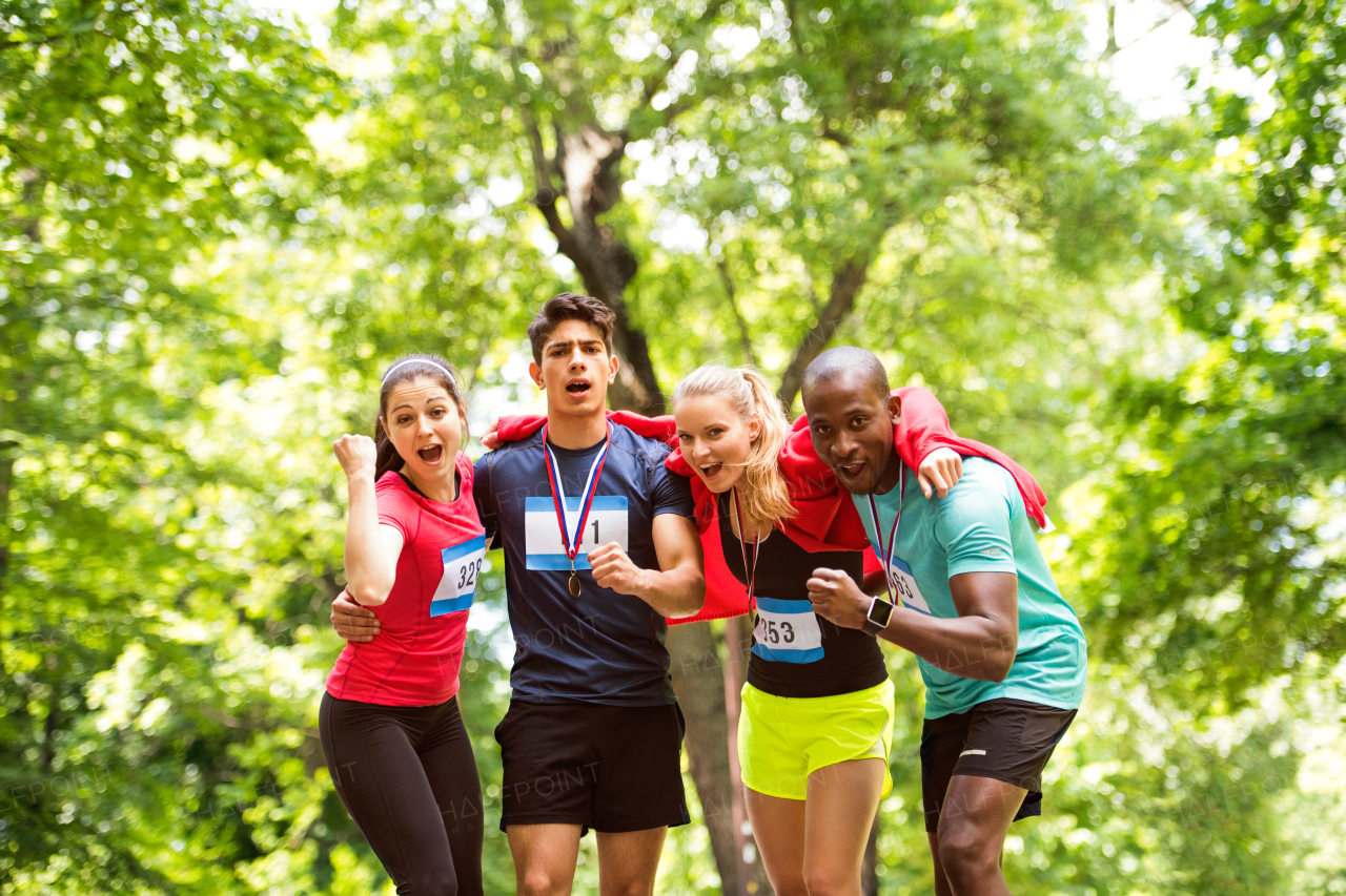 Group of young fit friends at the finish line happy after completing race. Green sunny park.