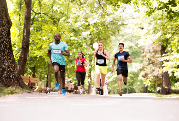 Group of young athletes running in green sunny summer park.