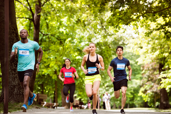 Group of young athletes running in green sunny summer park.