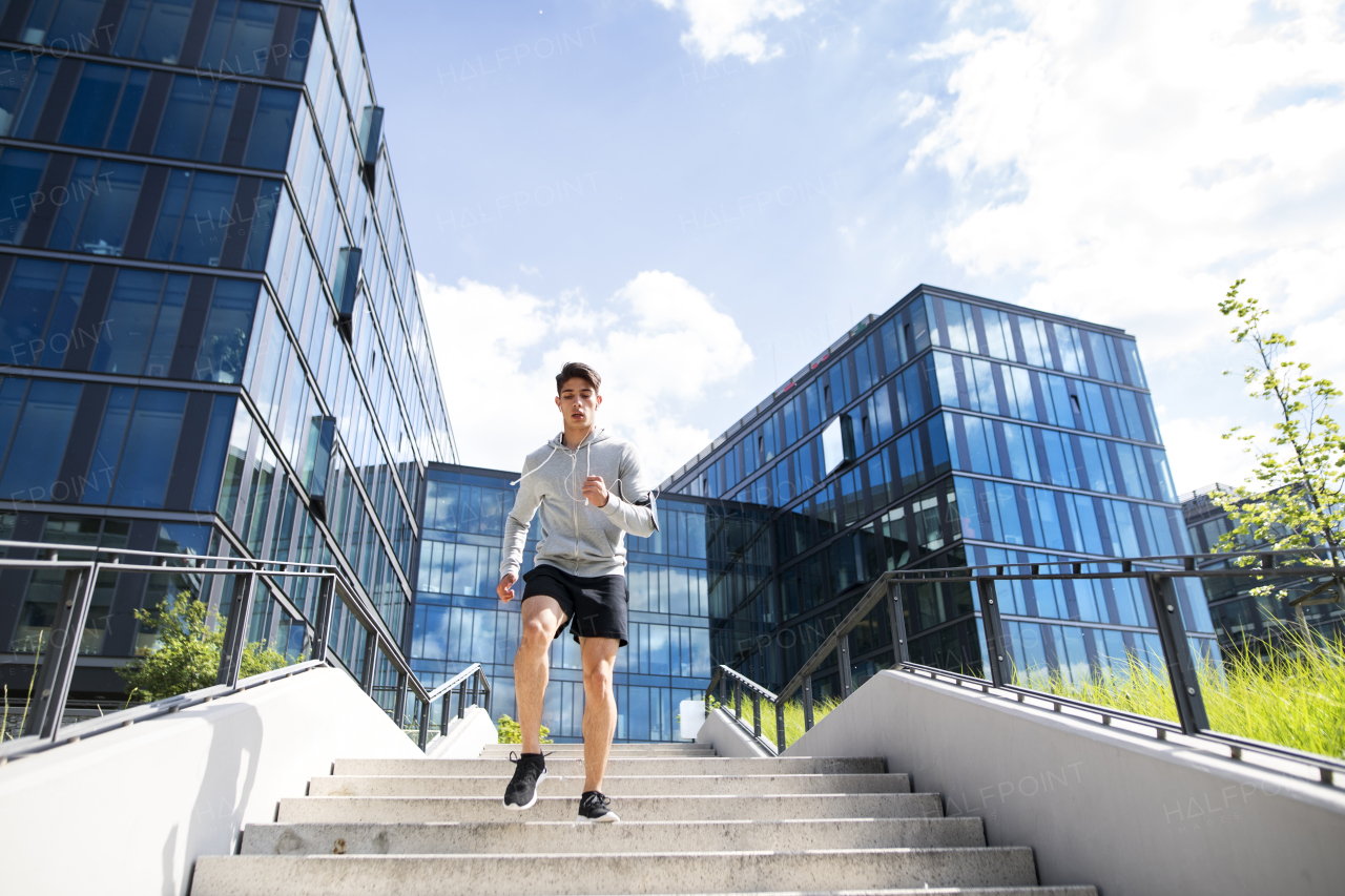 Young athlete in the city running on stairs in front of glass buildings.