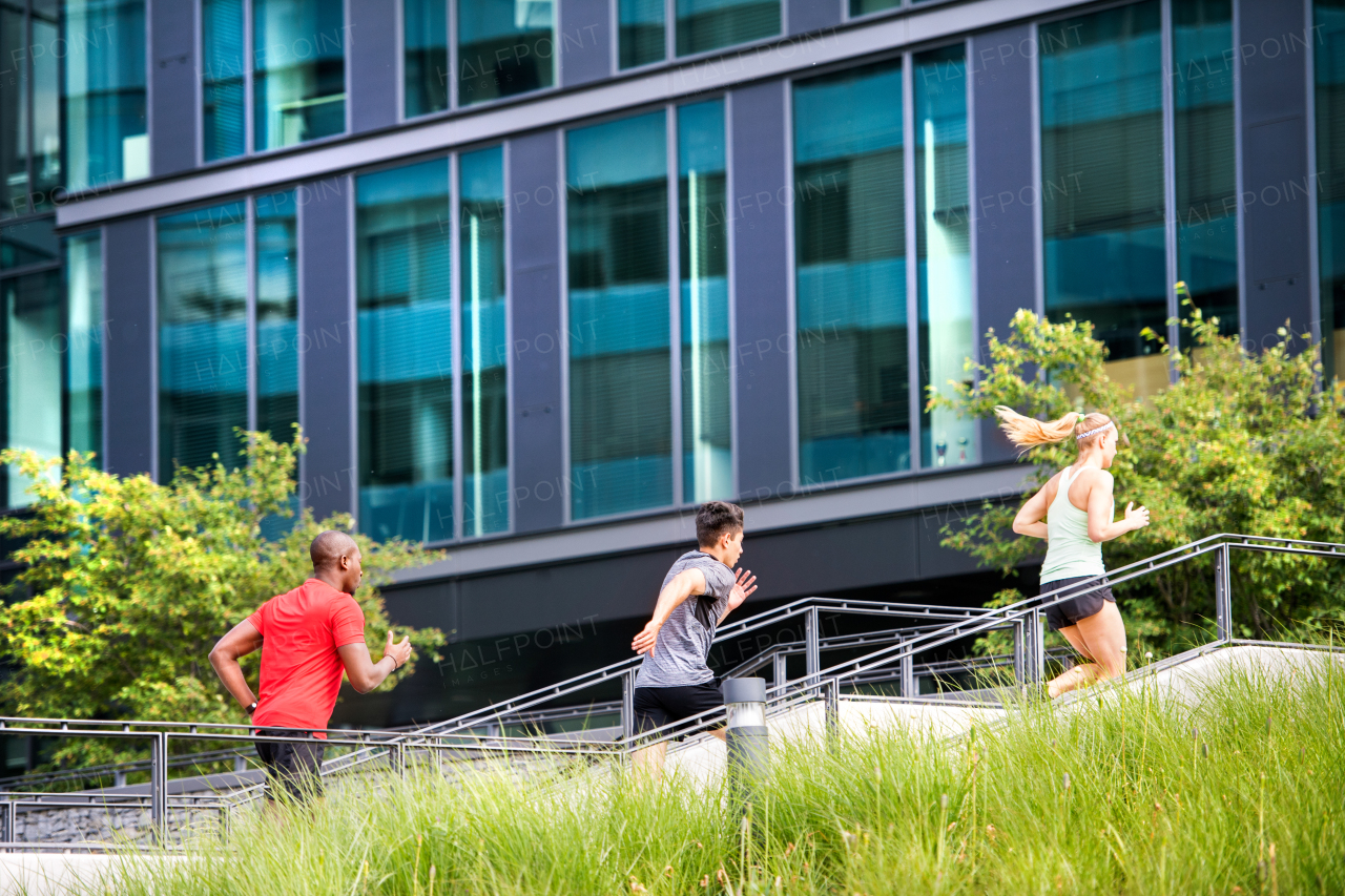 Beautiful young people in the city running together up the stairs in front of glass building.