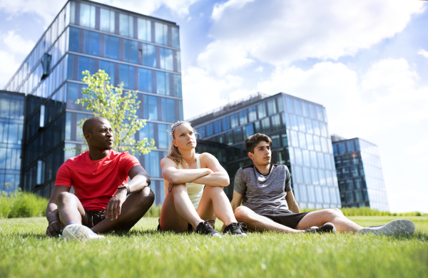 Beautiful young people together in the city. Runners resting in front of glass buildings.