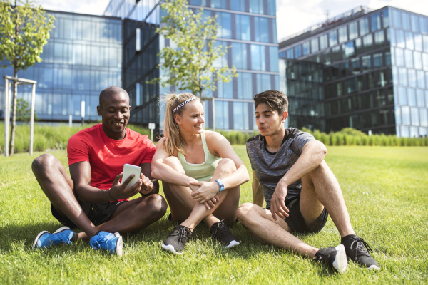 Beautiful young people together in the city. Runners with smartphone resting in front of glass buildings.