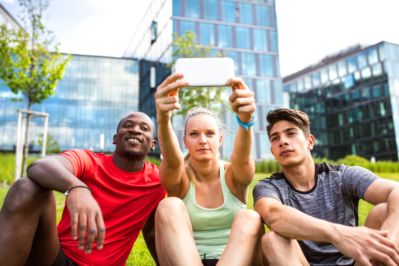 Beautiful young runners together in the city taking selfie with smart phone in front of glass buildings.