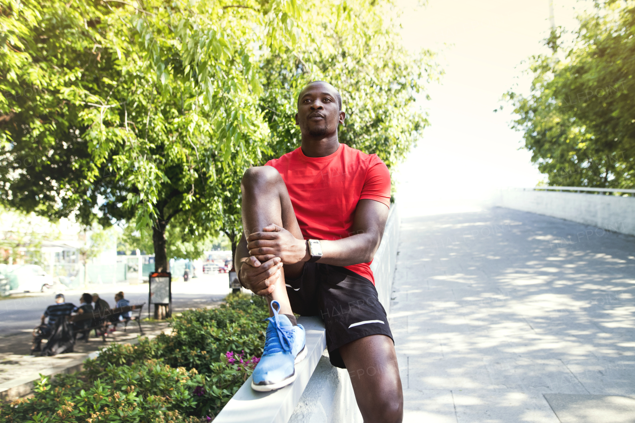 Young afro-american runner in the city sitting on the concrete wall, resting.