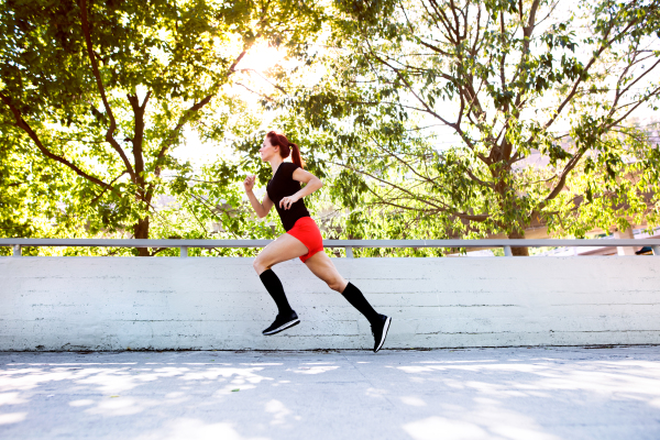 Beautiful young athlete in sports clothe running on concrete path in the city.