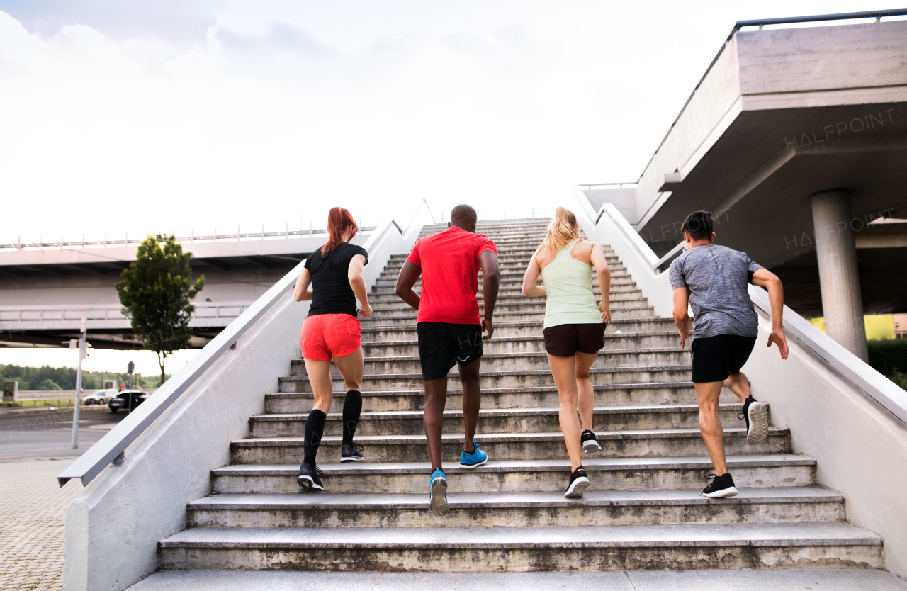 Beautiful young people in the city running together up the stairs, rear view.