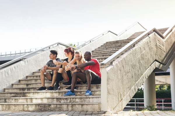 Beautiful young runners in the city together sitting on the stairs, looking at smart watch or smart phone, tracking their progress in running.