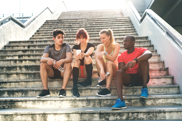 Beautiful young runners in the city together sitting on the stairs, looking at smart phone, tracking their progress in running.