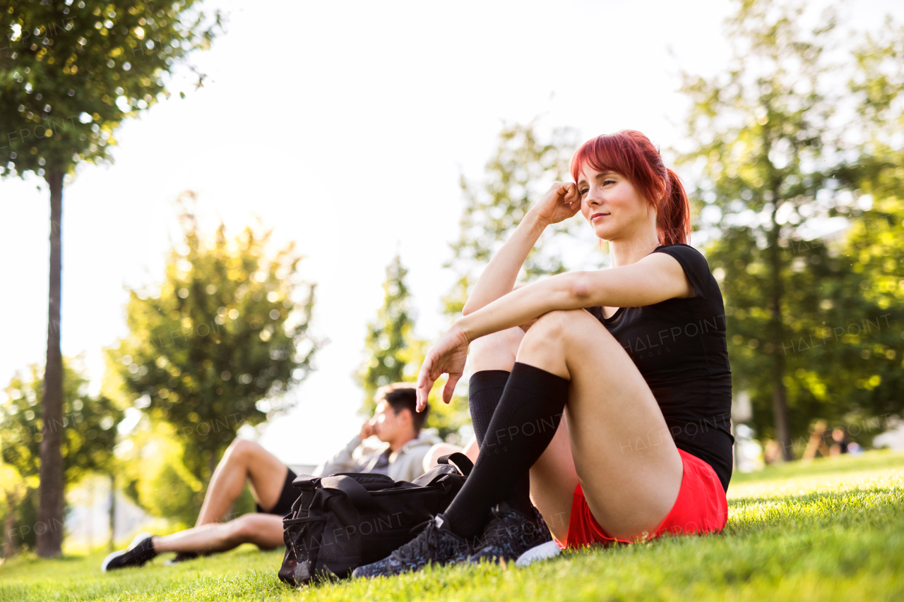 Beautiful young runner in the city sitting on the grass in park, resting.