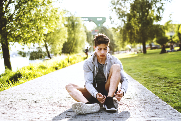 Young hispanic runner in the city sitting on concrete path tying his shoelaces.