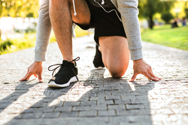 Unrecognizable young runner in starting position running in the city park.