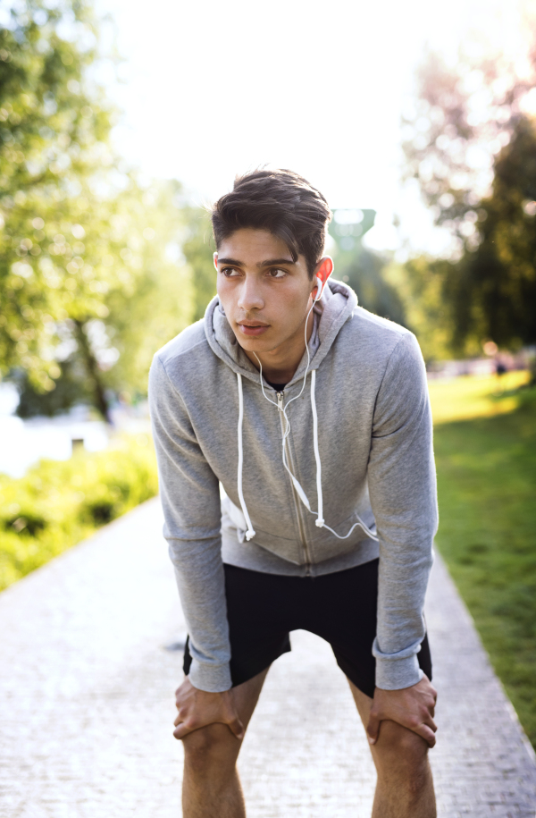 Handsome young runner in the city park, resting, earphones in his ears, listening to music.