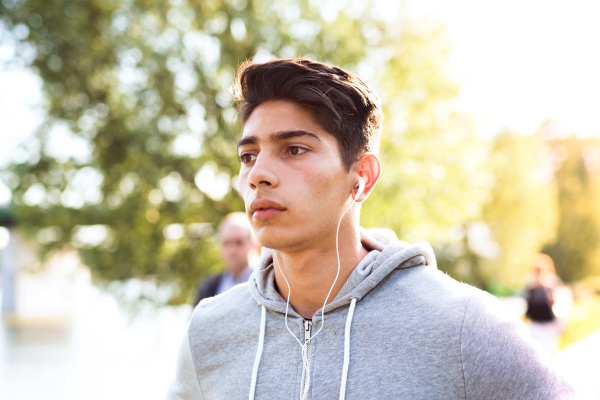 Handsome young runner in the city park, resting, earphones in his ears, listening music.