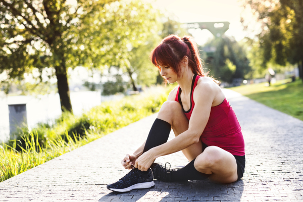 Young female runner in the city sitting on concrete path tying her shoelaces.