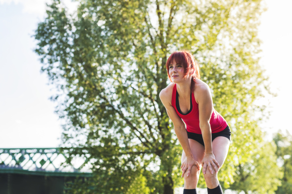 Beautiful young runner in sports clothes running in the city park, resting.