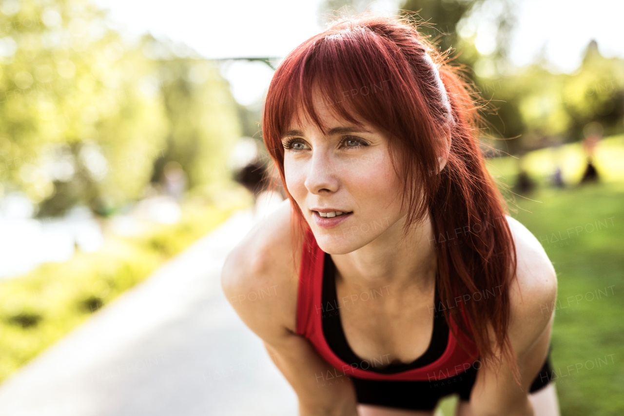 Beautiful young runner in sports clothes running in the city park, resting.