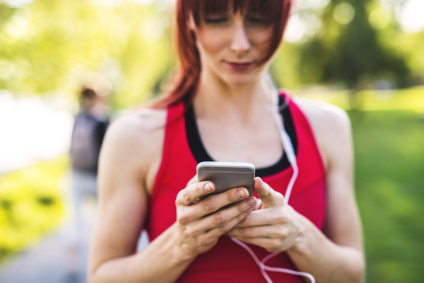 Beautiful young runner in park holding smart phone, listening to music.