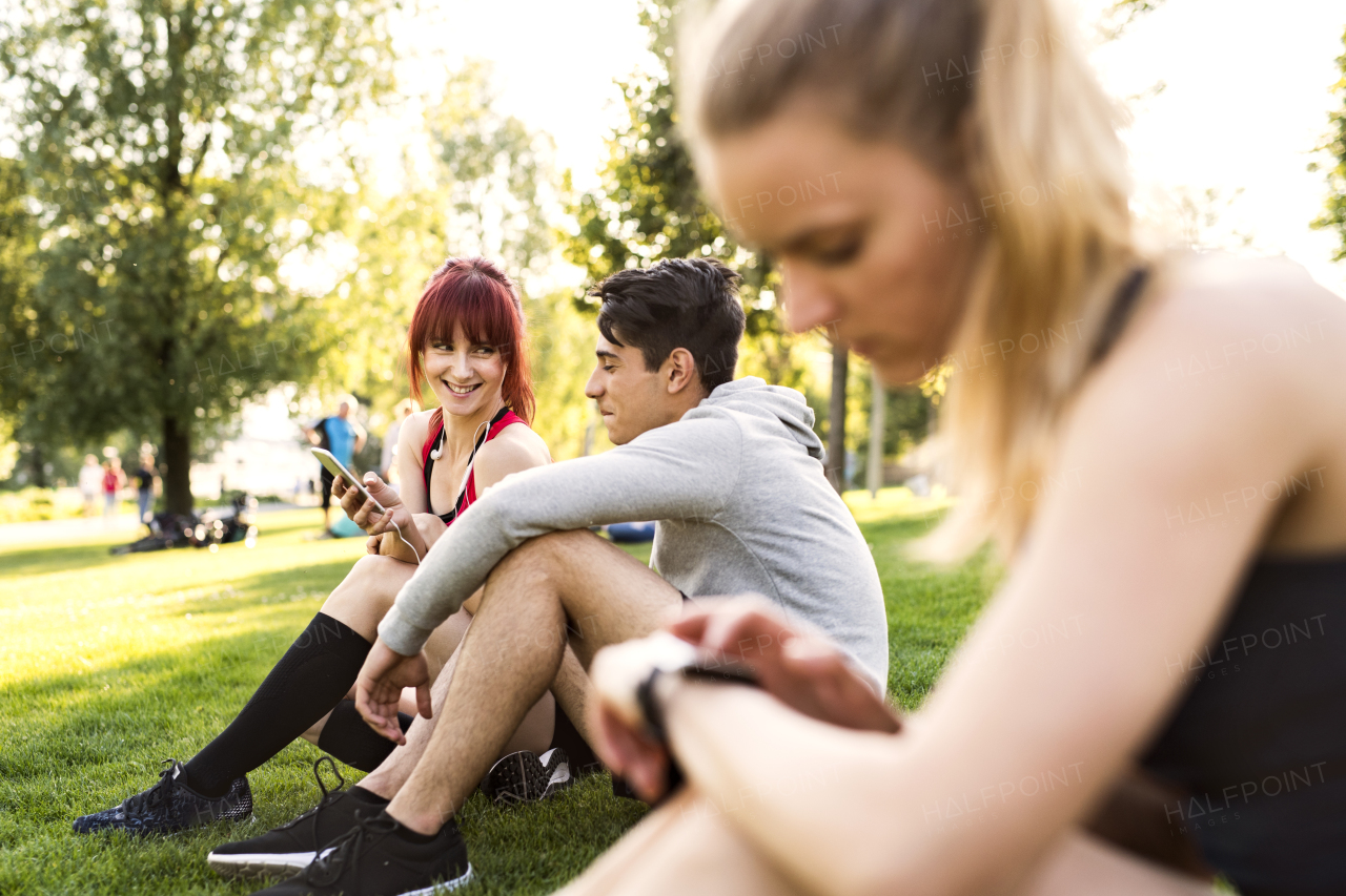 Group of young runners with smartphone resting in nature.