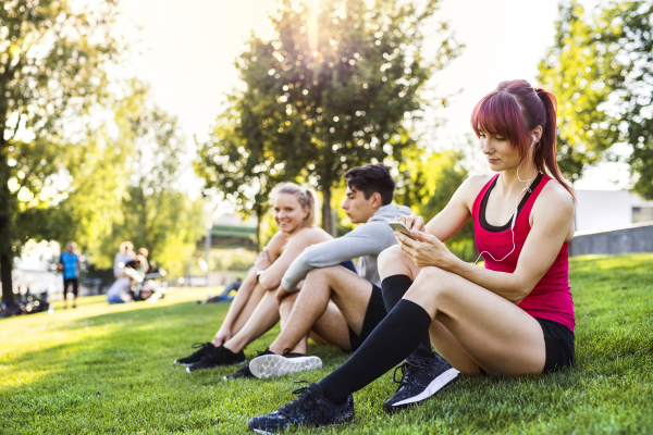 Group of young runners with smartphone resting in nature.