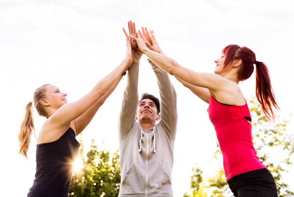 Group of young runners in park giving high five after completing exercise. Teamwork gesture.