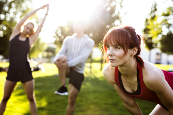 Group of young runners in nature warming up and stretching arms and legs.