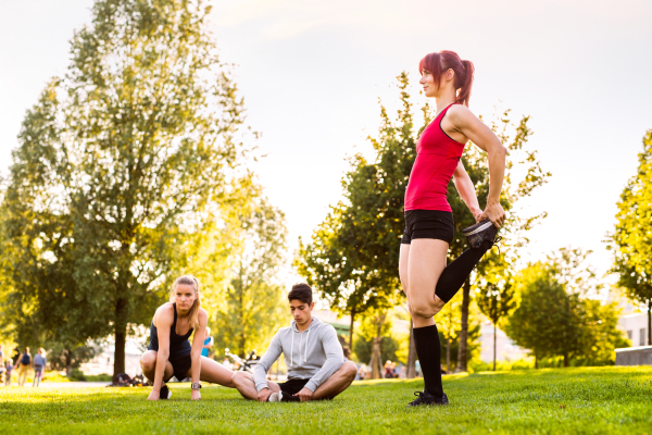 Group of young runners in nature warming up and stretching arms and legs.